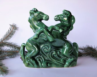 May include: A glossy, emerald green ceramic sculpture of two rearing horses. The horses are intertwined, with detailed manes and a swirling base. The sculpture is a decorative piece, likely for a shelf or tabletop.