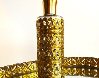 May include: A vintage perfume bottle with a gold-colored filigree overlay. The bottle has a clear glass body and a gold-colored cap. The filigree design is ornate and detailed, adding a touch of elegance. The bottle is displayed on a mirrored surface.