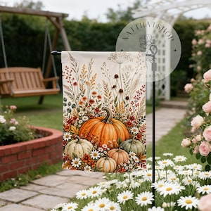 May include: A rectangular garden flag featuring a vibrant illustration of orange, white, and green pumpkins nestled among autumn wildflowers, dried grasses, and berries. The design is set against a cream background with a floral watermark logo.