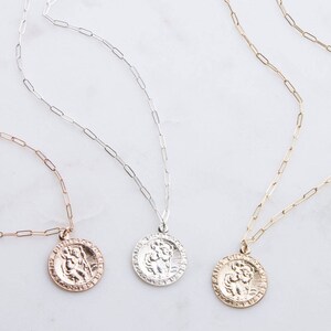 May include: Three gold, silver, and rose gold necklaces with a Saint Michael pendant. Each necklace features a delicate paperclip chain.