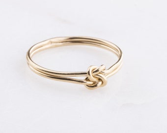May include: A gold knot ring with a simple design. The ring is made of two bands of wire that are twisted together to form a knot.