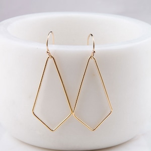 May include: A pair of gold geometric earrings with a diamond shape. The earrings are made of thin wire and have a simple, modern design.