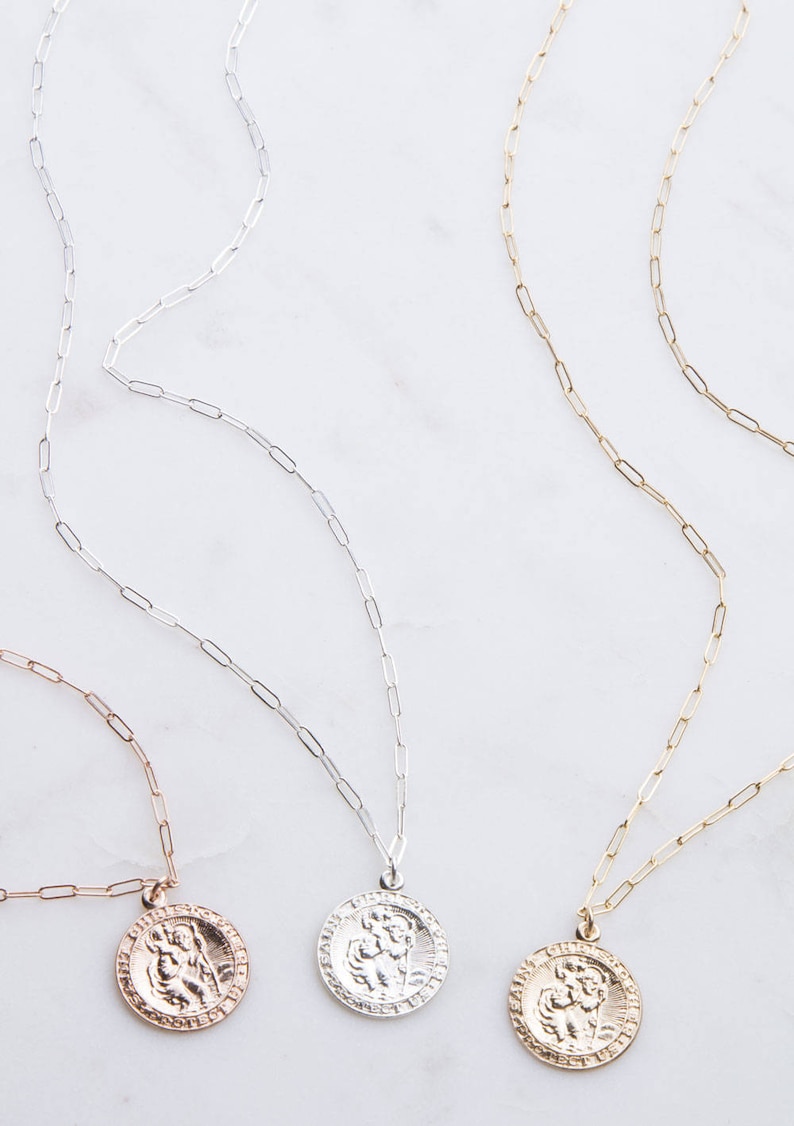 May include: Three gold, silver, and rose gold necklaces with a Saint Michael pendant. Each necklace features a delicate paperclip chain.