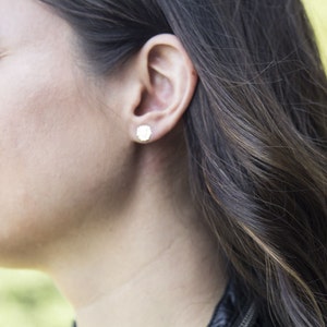 May include: A close-up of a woman's ear with a small, round, white earring. The woman has long, dark brown hair.
