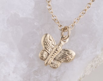 Pode incluir: Um colar de ouro com um pingente de borboleta em um fundo branco.
