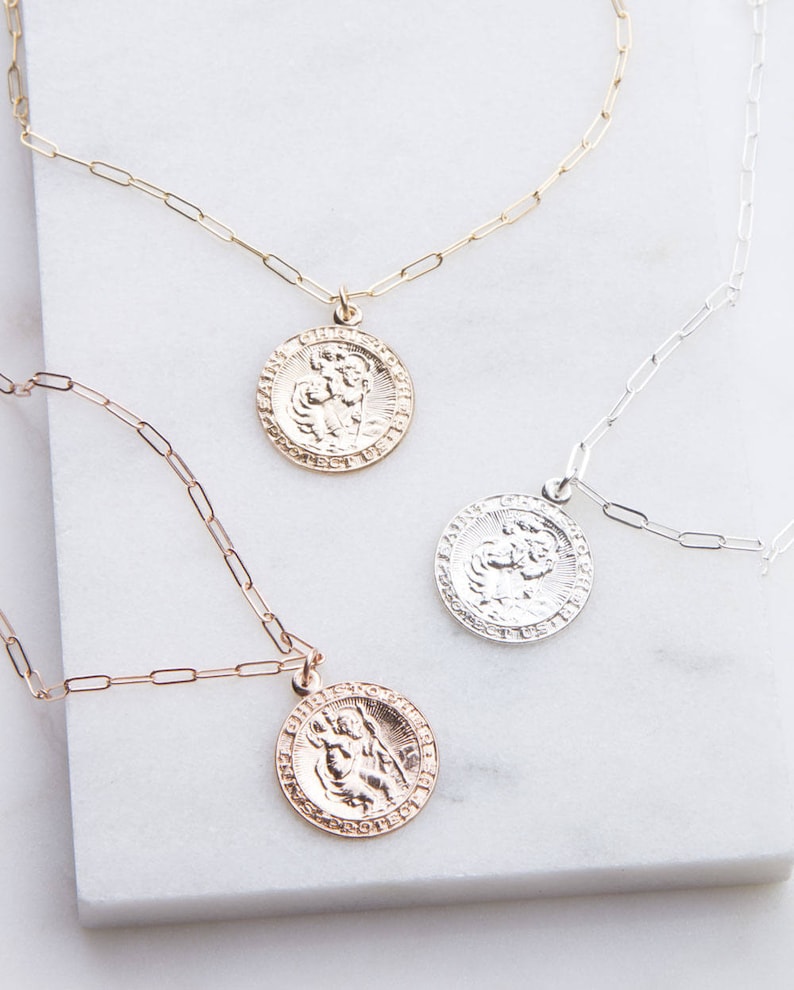 May include: Three gold, silver, and rose gold necklaces with Saint Christopher medallions. Each necklace features a delicate chain and a round medallion with a detailed image of Saint Christopher carrying a child.