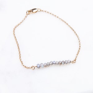 May include: A delicate gold chain bracelet with a row of iridescent grey labradorite gemstones.