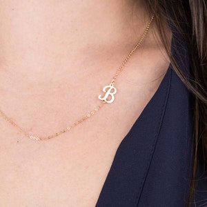 May include: A gold chain necklace with a delicate cursive letter 'B' pendant.