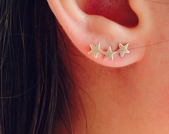 Puede incluir: Primer plano de la oreja de una persona con tres pendientes de estrella de oro.