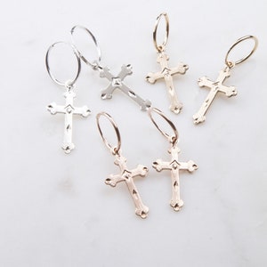 May include: Five pairs of hoop earrings with a cross charm. The earrings are available in gold, rose gold, and silver.