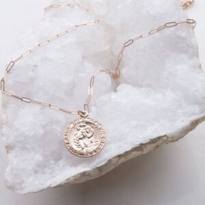 May include: A gold chain necklace with a round pendant featuring a religious image of Saint Christopher. The pendant has an inscription around the edge.