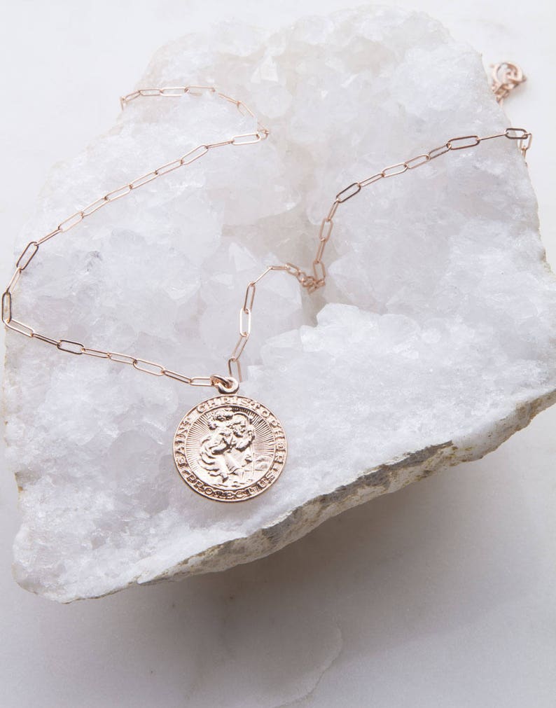 May include: A gold chain necklace with a round pendant featuring a religious image of Saint Christopher. The pendant has an inscription around the edge.