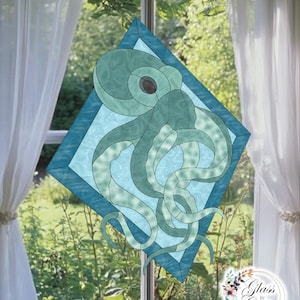 Puede incluir: Vidriera con un diseño de pulpo turquesa dentro de un marco en forma de diamante. El pulpo tiene tentáculos detallados y un ojo oscuro. El marco es de un tono más oscuro de turquesa. El fondo muestra una ventana con cortinas blancas y vegetación.