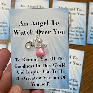 May include: A card with the text "An Angel To Watch Over You" and a small angel charm. The angel charm has a pink heart-shaped body and silver wings. The card also includes inspirational text.
