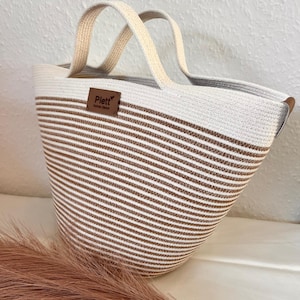 May include: A white and brown striped rope tote bag with a brown leather tag that says "Plett Home Decor".