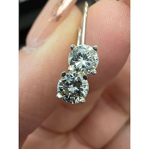 Op de afbeelding: Een paar zilveren oorbellen met twee ronde, briljant geslepen diamanten. De diamanten zijn gezet in een klassieke prong-zetting, die hun schittering benadrukt. De oorbellen hebben een klapsluiting.