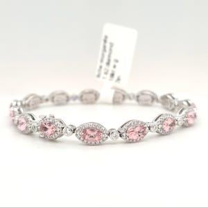 May include: A delicate bracelet featuring oval-shaped pink gemstones, each surrounded by a halo of small, clear stones. The bracelet is made of silver-colored metal and is displayed against a white background. A tag is attached.