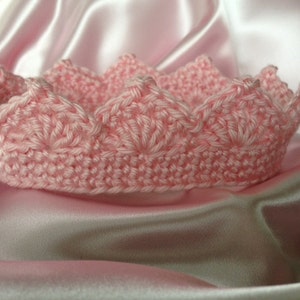 May include: A pink crocheted crown with a scalloped edge. The crown is made with a delicate stitch pattern and is perfect for a princess.