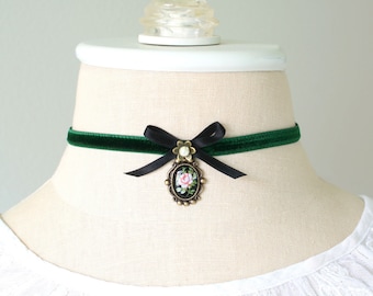 Op de afbeelding: Een groene fluwelen choker met een zwarte satijnen strik en een gouden hanger met een roze roos.
