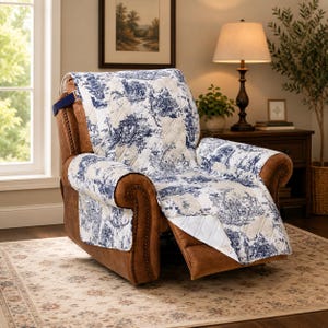 May include: A brown leather recliner chair with a blue and white toile print quilted cover. The cover features a repeating pattern of pastoral scenes. The chair is in a well-lit room with a rug and a lamp.