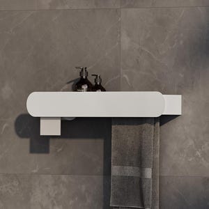 Puede incluir: Un estante de pared blanco con extremos redondeados, que presenta un soporte rectangular en el lado izquierdo. Dos botellas con dosificador de color marrón oscuro descansan sobre la superficie y una toalla gris cuelga del lado derecho.