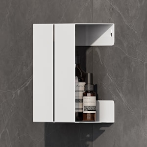 May include: A white metal wall-mounted storage shelf with a vertical slit design. The shelf holds two amber glass bottles with black pump and spray nozzles, featuring labels that read Aesop and Herbal Deodorant Déodorant Herbes.