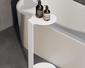 May include: A white metal C-shaped side table with a circular top and base, featuring a tall vertical support. Two amber-colored glass pump bottles with black dispensers and white labels are placed on the top surface of the table.
