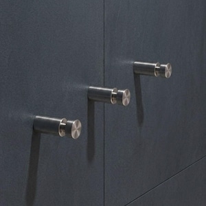 Peut inclure: Trois patères murales cylindriques en métal avec une finition brossée, montées horizontalement sur une surface texturée gris foncé. Chaque crochet présente un embout circulaire plat et un corps tubulaire lisse, disposés en diagonale.