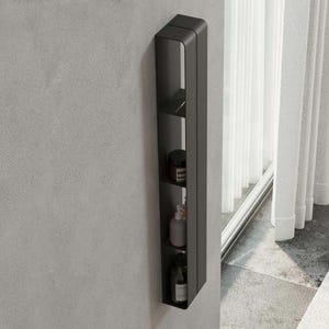 May include: A tall, vertical, matte black wall-mounted storage unit featuring four open shelves. The shelves contain various small cylindrical containers and bottles, including a dark jar, a white bottle, and a clear glass bottle with a pump.