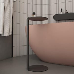 May include: A matte black metal side table featuring a slender vertical support, a circular base, and a matching circular top surface. The table is positioned next to a curved, solid light pink bathtub in a bathroom with white tiled walls.