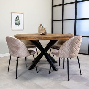 May include: A round wooden dining table with a black metal X-shaped base. Four beige velvet chairs with black metal legs surround the table.