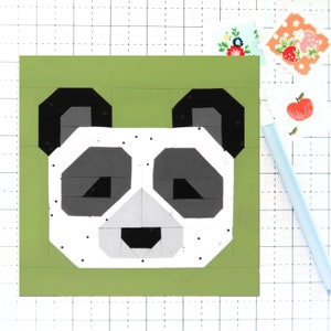 Op de afbeelding: Een groen vierkant van stof met een zwarte en witte panda-gezichtsapplicatie. De panda heeft zwarte ogen, een zwarte neus en witte vacht met zwarte stippen.