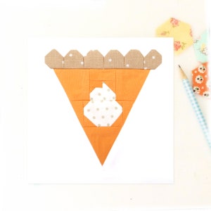 Puede incluir: Un bloque de colcha de retazos en forma de pastel con una corteza marrón y un relleno naranja. El relleno tiene un diseño blanco con lunares en el centro.