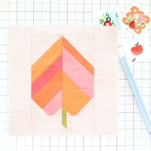 Puede incluir: Un bloque de hoja de tela rosa y naranja para una colcha. La hoja está hecha de varios cuadrados de tela cosidos juntos para crear un patrón geométrico.