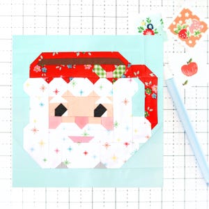 May include: A patchwork quilt block featuring a Santa Claus face with a red hat, white beard, and a white background with colorful stars. The block is on a light blue background.