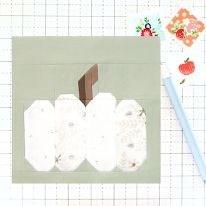 May include: A white pumpkin with a brown stem, made from fabric scraps, on a green background. The pumpkin is decorated with a floral pattern.