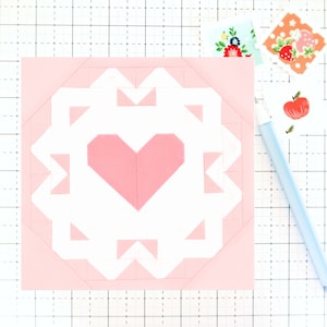 May include: A pink and white patchwork quilt block with a heart in the center. The heart is made of pink fabric and is surrounded by a white border. The border is made of small triangles of pink and white fabric.