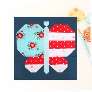 Op de afbeelding: Een blauwe, vlindervormige quiltblok met rode, witte en blauwe stof. De vlinder heeft aan de ene kant een bloemenpatroon en aan de andere kant een gestreept patroon.