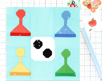 May include: A blue, green, yellow, and red fabric applique design on a light blue background. The design features four geometric shapes with rounded tops and a white circle with two black circles inside.