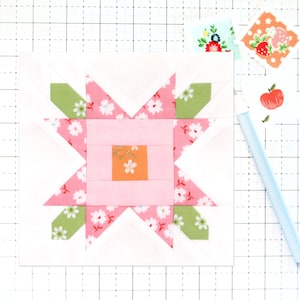 May include: A pink and white patchwork quilt block with a green and white star design. The block is made up of squares and triangles, and the centre square is a light orange colour with a floral pattern.