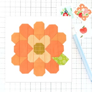 May include: A patchwork flower block in shades of orange, yellow, and green. The flower is made up of multiple fabric squares sewn together to create a geometric design.