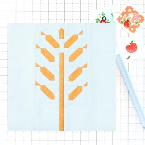 May include: A light blue and orange quilt block with a tree design. The tree trunk is orange with a dotted pattern, and the branches are orange with white polka dots. The background is light blue.