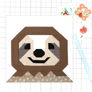 May include: A brown and beige patchwork sloth face with a white and brown patterned fabric on the bottom. The sloth has a black nose and eyes.
