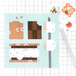 May include: A light blue background with a brown, white, and grey s'more design. The s'more is made of a brown graham cracker, two white marshmallows, and a brown chocolate bar.