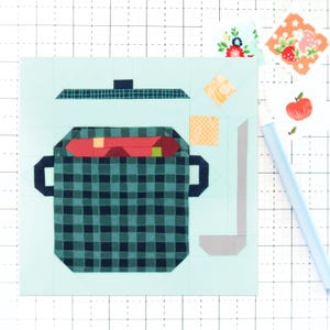 Puede incluir: Una olla de cuadros azules y verdes con una tapa roja y un cucharón gris. La olla está llena de cuadrados de tela roja y amarilla.