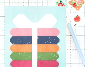 May include: A light blue fabric square with a white bow and a stack of colorful fabric strips with different patterns. The fabric strips are pink, navy blue with white dots, orange, green with white dots, and pink.
