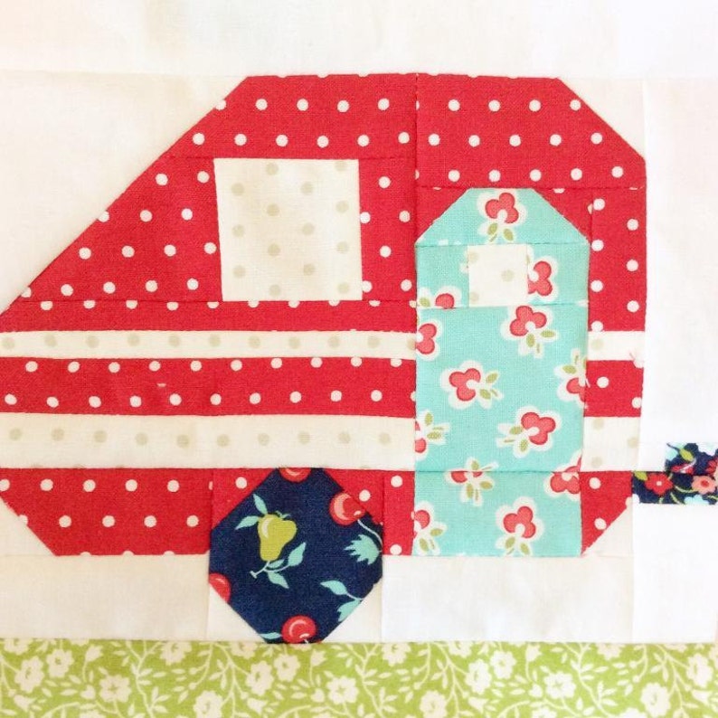May include: A red and white polka dot camper with a blue and white floral door and a blue and white wheel with a pear and cherry pattern. The camper is on a white background with a green and white floral pattern below.