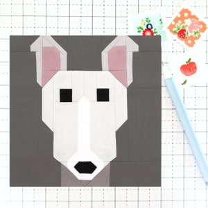May include: A gray, white, and pink fabric block depicting a dog's face. The dog has black eyes and a black nose.