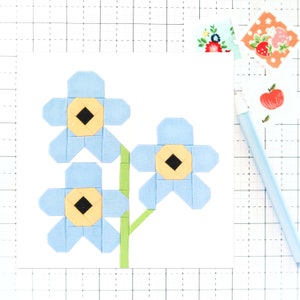 May include: A blue fabric flower with a yellow center and a black center, with two other blue fabric flowers with yellow and black centers, on a green stem.