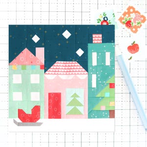 May include: A patchwork quilt block featuring a winter village scene with houses, a tree, and a sled. The houses are pink, green, and blue with white accents. The tree is green with a blue and white star on top. The sled is red with a white base. The background is a dark blue fabric with white stars.